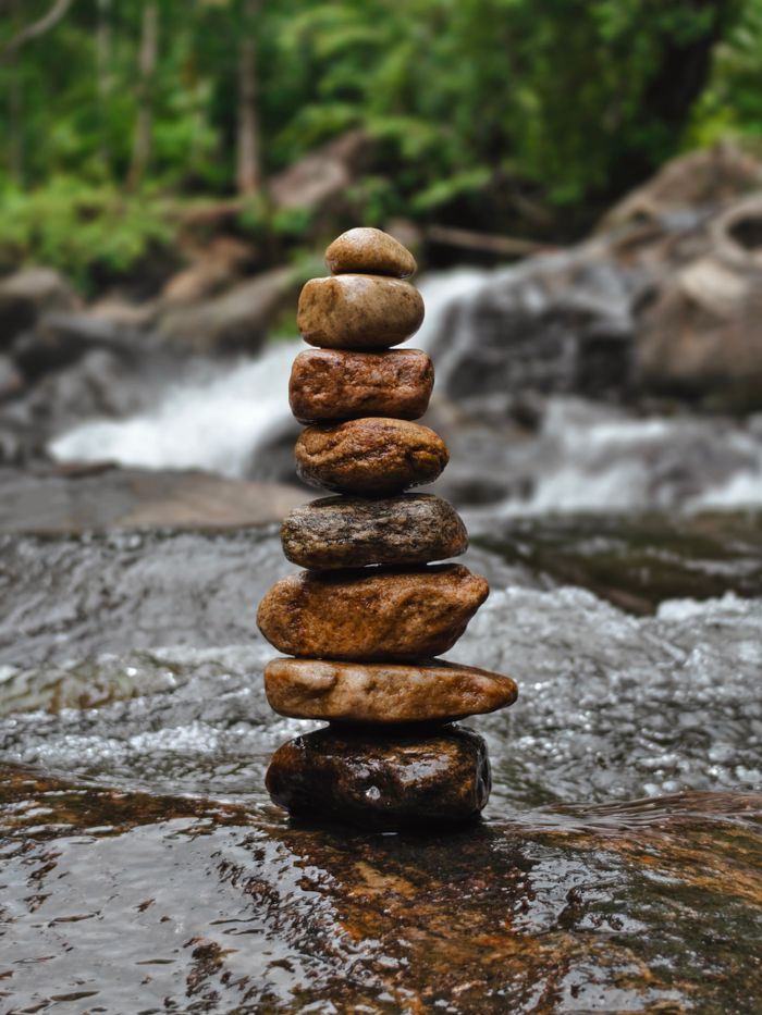 Carefully balanced stack of stones by a flowing stream in a serene forest setting.
