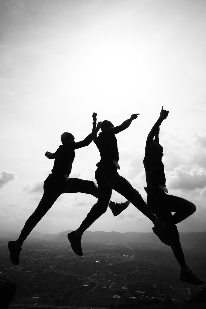 Black and white of carefree friends jumping high over large town under cloudy sunny sky