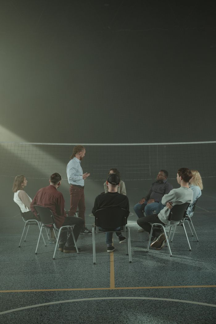 Adults participating in a group therapy session in a gymnasium, promoting mental health and peer support.